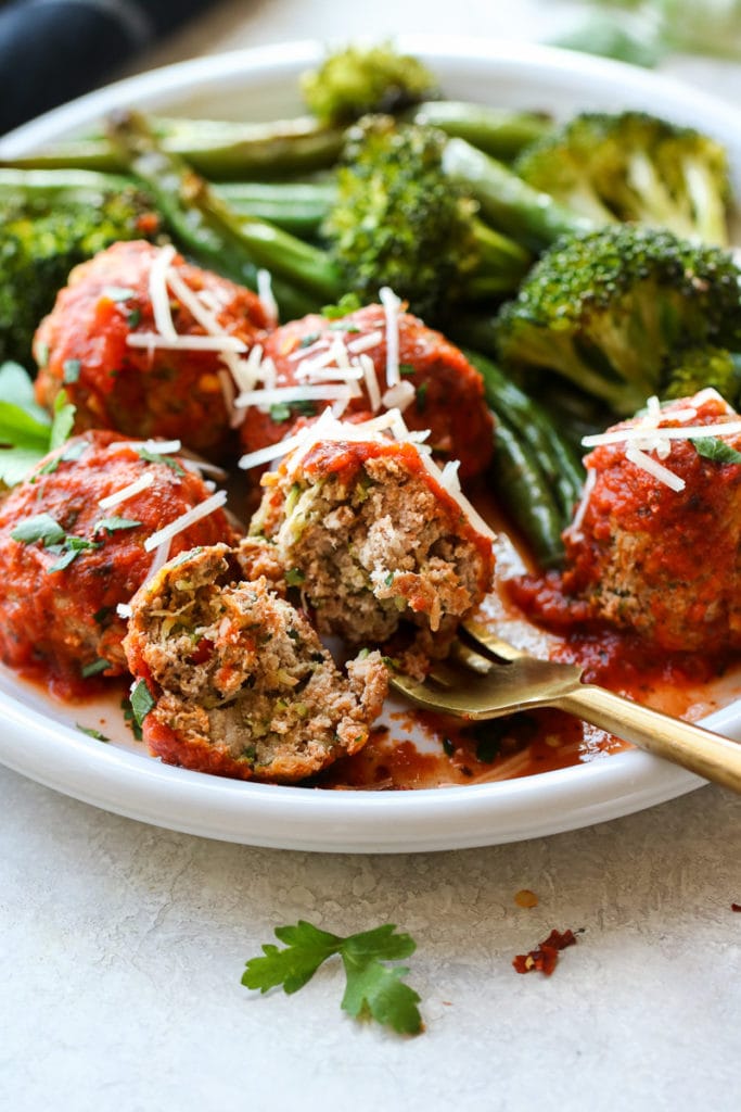 Turkey Zucchini Meatballs on a white plate with broccoli and green beans.