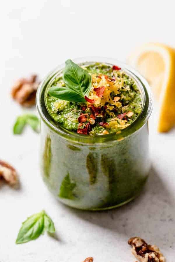 Basil walnut pesto in a small jar topped with lemon zest, basil sprig, and red pepper flakes.