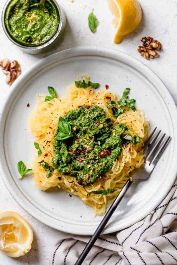 Overhead view of spaghetti squash noodles topped with homemade basil walnut pesto on a white plate