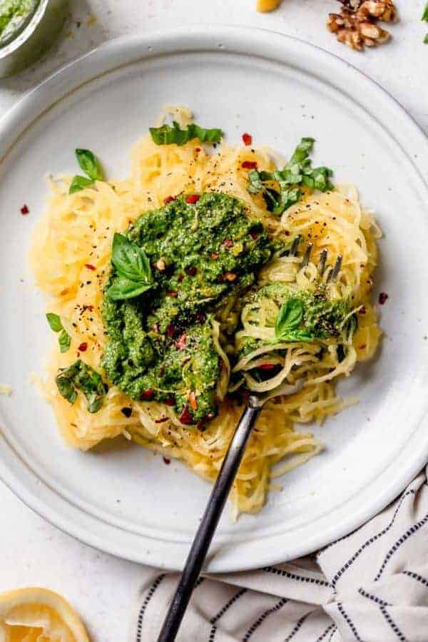 Spaghetti squash noodles topped with basil walnut pesto plated on a cream colored plate
