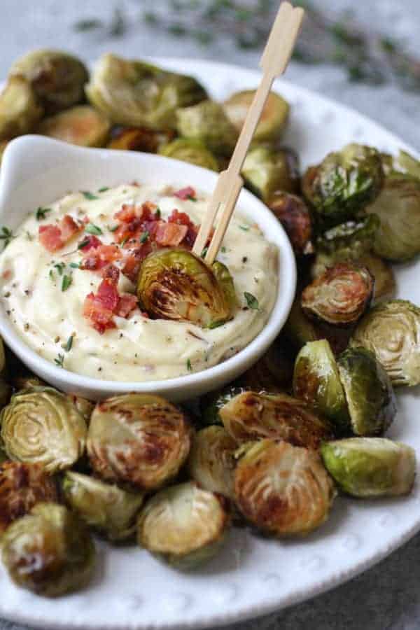Roasted Brussels Sprout being dipped in Bacon Aioli on a white plate