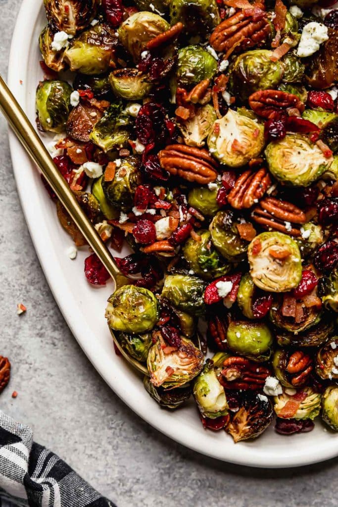  Roasted Brussel Sprouts with Bacon and Balsamic on a white serving platter with a gold serving spoon.