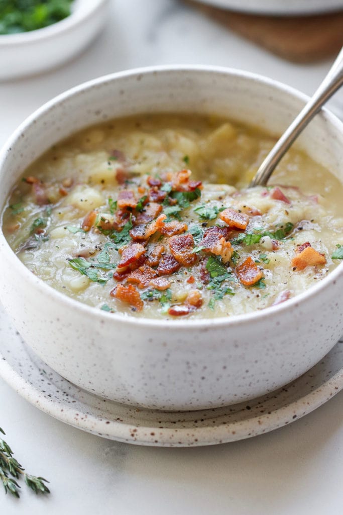 Creamy potato leek soup in a speckled bowl topped with chives and bacon