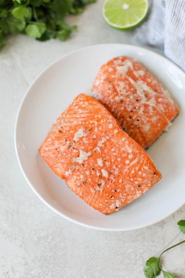 Two perfectly grilled, bright red filets of sockeye salmon on a white plate that have been seasoned with salt and pepper to make Grilled Salmon with Elote Style Veggies.