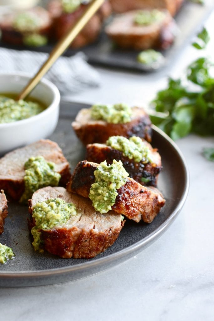 Grilled Pork Tenderloin sliced and topped with avocado green sauce. Served on a gray plate. 
