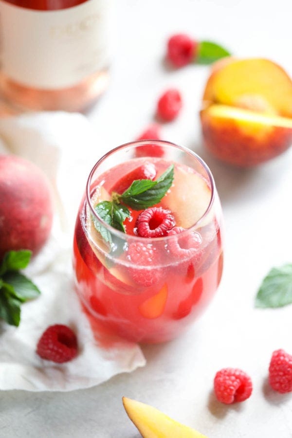 這款覆盆子桃桃玫瑰桑格利亞汽酒正等待著一杯夏日，在這里白色餐桌上被新鮮水果包圍。