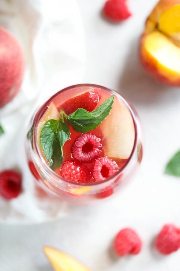 一杯覆盆子-桃桃玫瑰桑格利亞汽酒的俯視圖，上面有桃片，三個豐滿的漿果和一小撮薄荷漂浮在頂部。