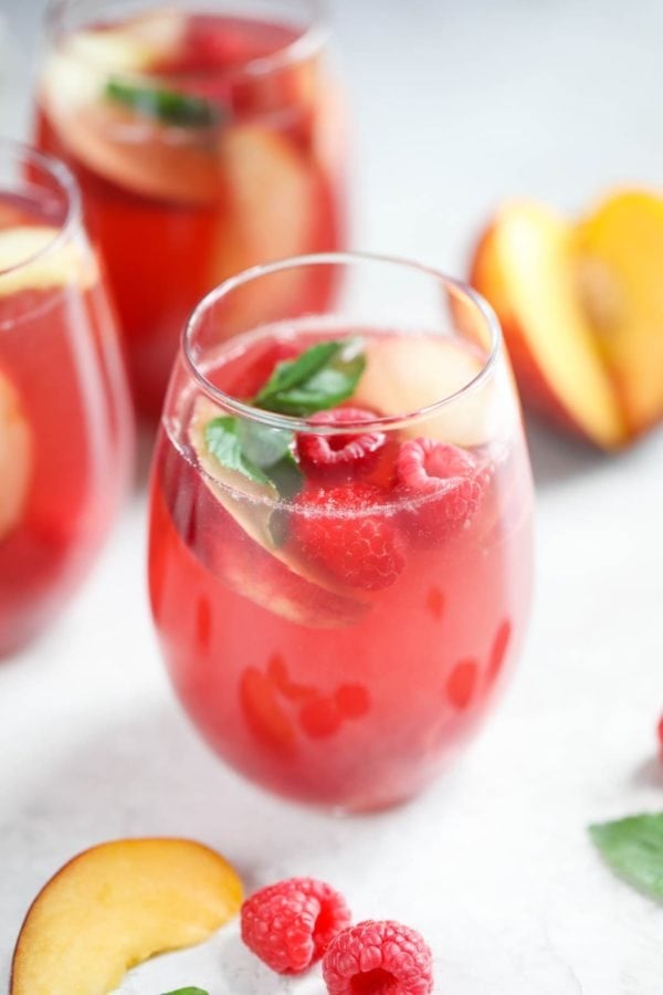 準備將三杯裝滿覆盆子-桃子玫瑰桑格利亞汽酒的無莖葡萄酒杯與朋友分享。