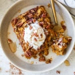 Gluten-free pumpkin baked oatmeal on a cream plate with a gold fork and topped with whipped cream and pecans.