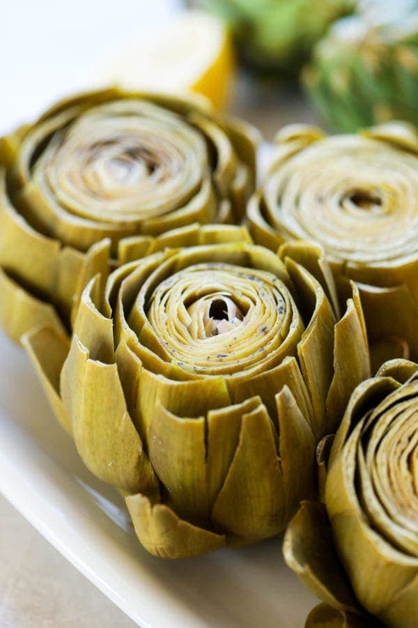 Freshly cooked artichokes with petals peeling away from the center on a white platter