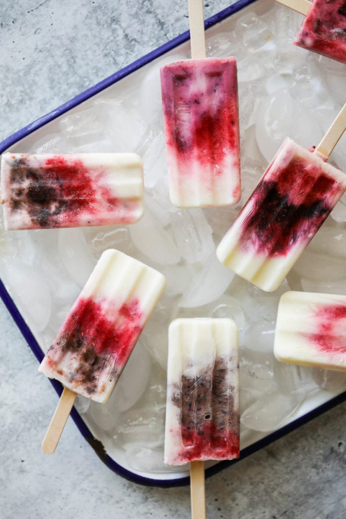 Several homemade yogurt popsicles with a berry swirl in a tray filled with ice cubes
