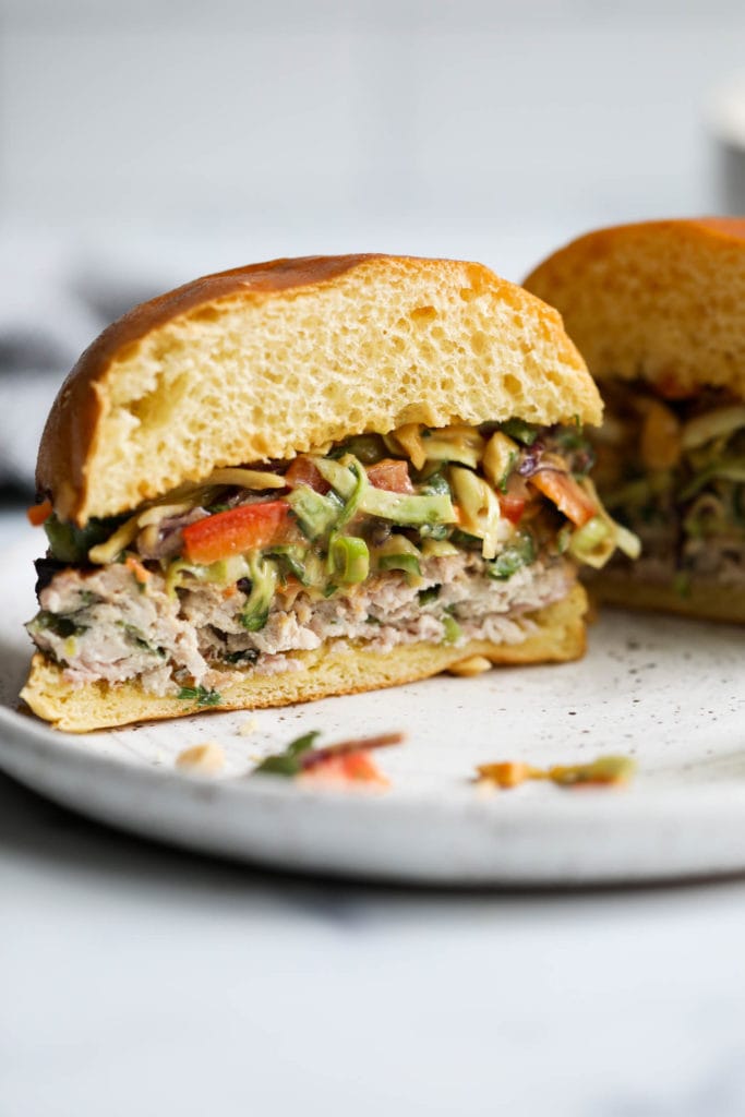 A grilled pork burger in a gluten-free bun and topped with creamy Thai slaw cut in half