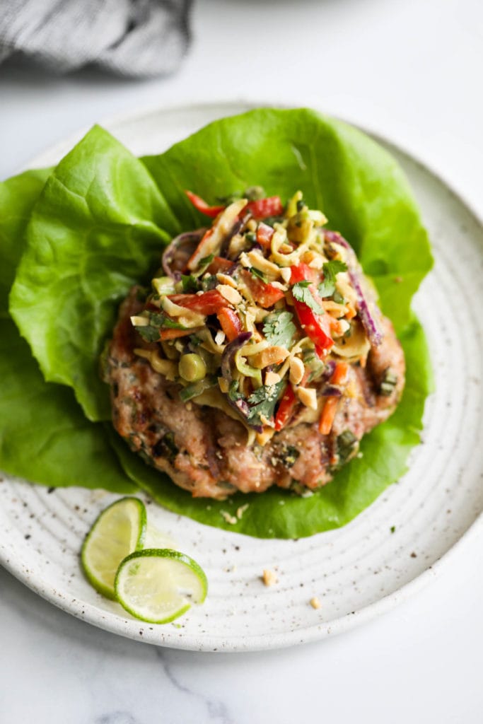 A grilled pork burger on two lettuce leaves and topped with creamy Thai slaw