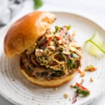 A grilled pork burger topped with creamy Thai Slaw in a gluten-free bun