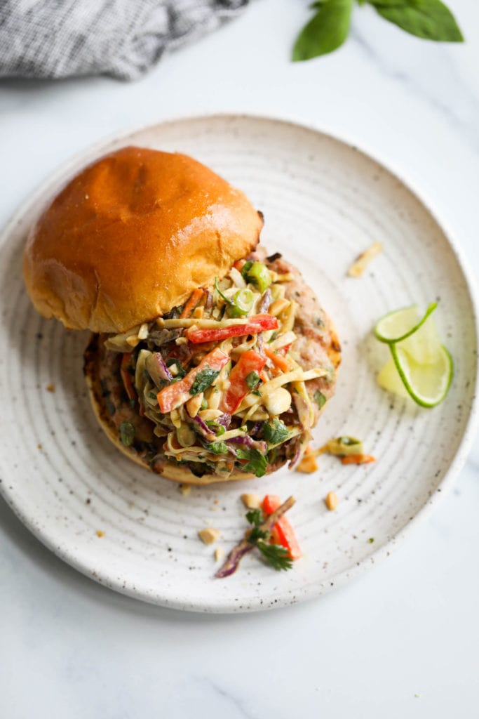 A grilled pork burger topped with creamy Thai-inspired slaw on a gluten-free toasted bun