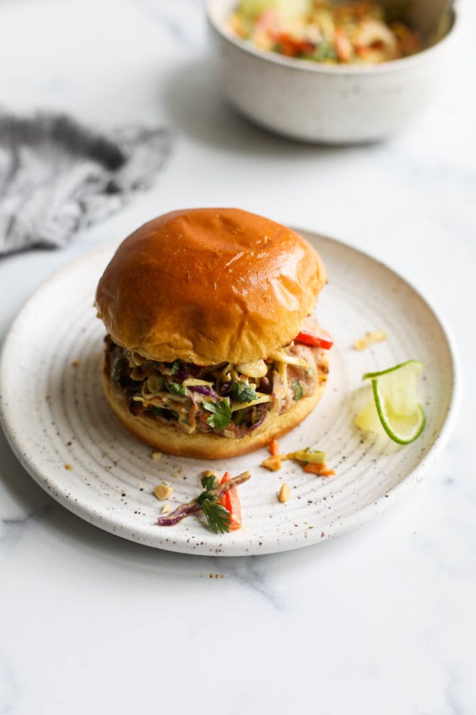 A grilled pork burger topped with creamy Thai slaw in a gluten-free toasted bun