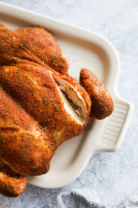 A smoked spatchcock chicken with paprika rub served on a white platter with a deep cut in the breast so show tender meat.