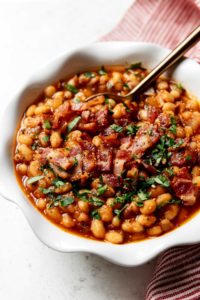 Instant Pot Baked Beans with bacon served in a white scalloped edge bowl with a gold spoon in the beans.
