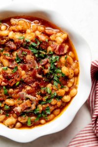 A bowl filled with Instant pot baked beans and topped with bacon crumbles and fresh herbs