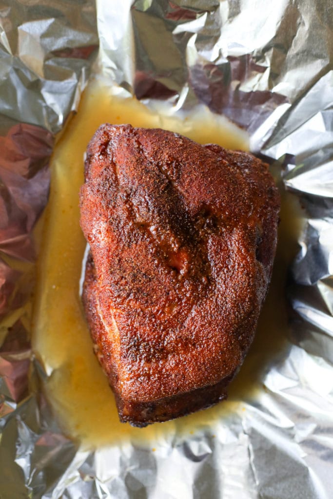 Grilled pork butt resting in foil with natural juices all around it
