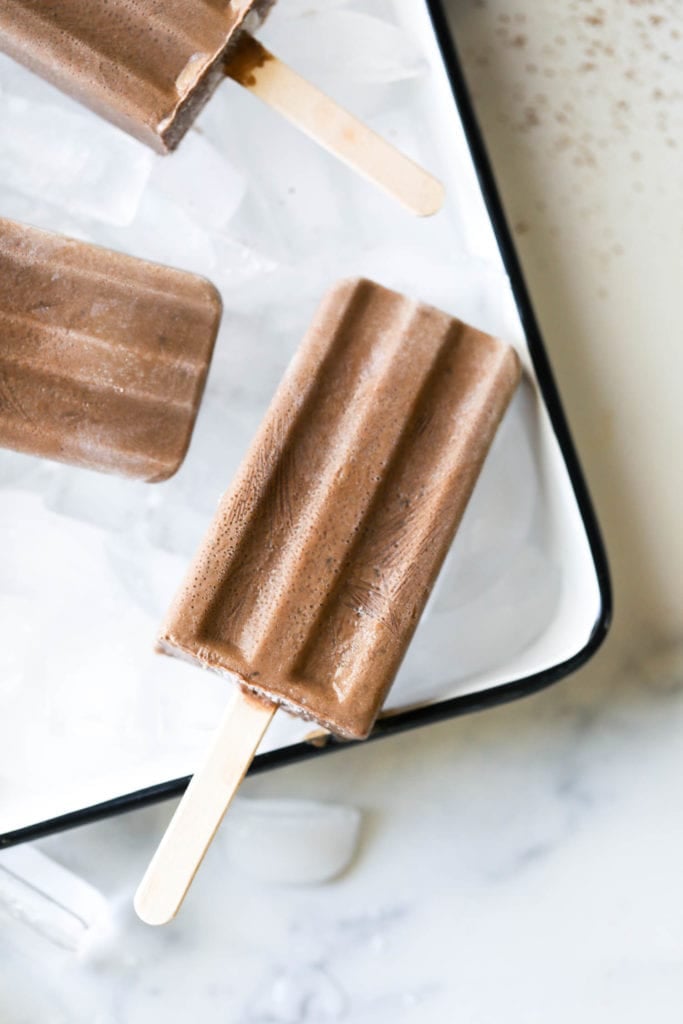 Creamy fudgesicles on a platter of ice with popsicle stick holders.
