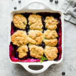 Gluten-free Blueberry Cobbler topped with nine soft golden biscuits in a white baking dish