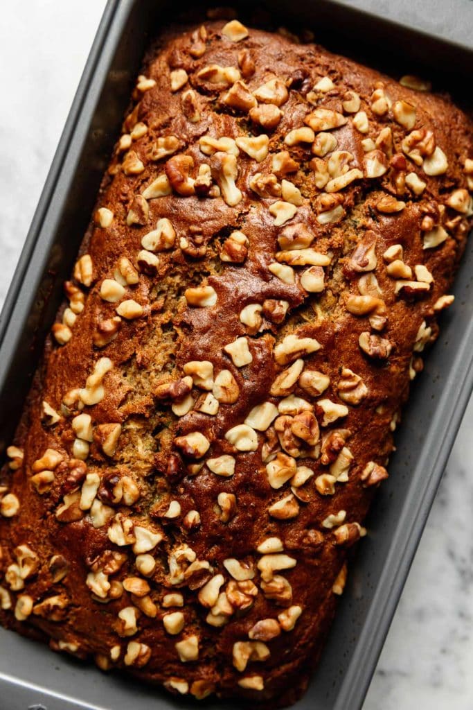 Freshly baked and golden brown gluten-free zucchini bread topped with walnuts in a loaf pan