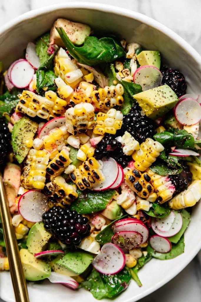 Charred corn, blackberries, sliced radishes, diced avocados over a bed of spinach in a white bowl