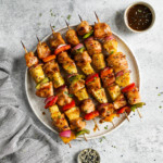Grilled teriyaki chicken pineapple kebabs lined up on a speckled plate