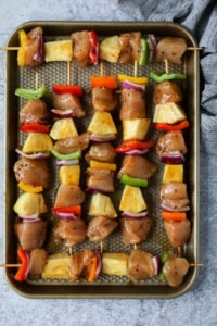 Pineapple chicken kebabs on skewers lined up on a baking sheet ready for the grill